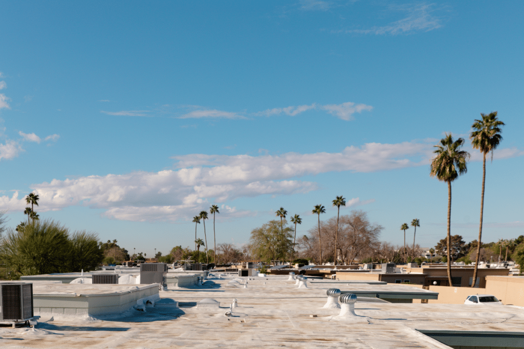 A Phoenix home with a white foam roof on a sunny day, surrounded by trees.