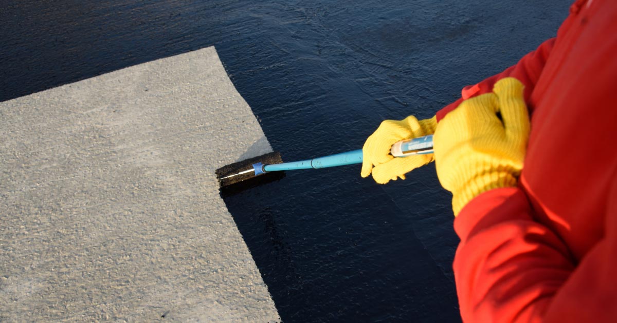 Worker applying thick black roof coating