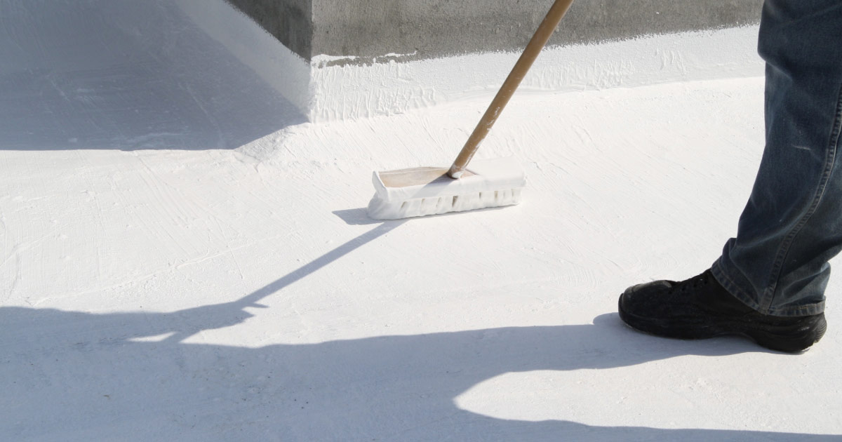 Roofer applying white coating on flat roof in Peoria